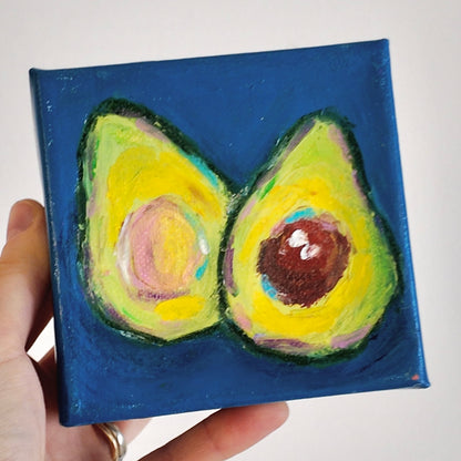 hand holding a painting of avocado cross section on a dark blue background