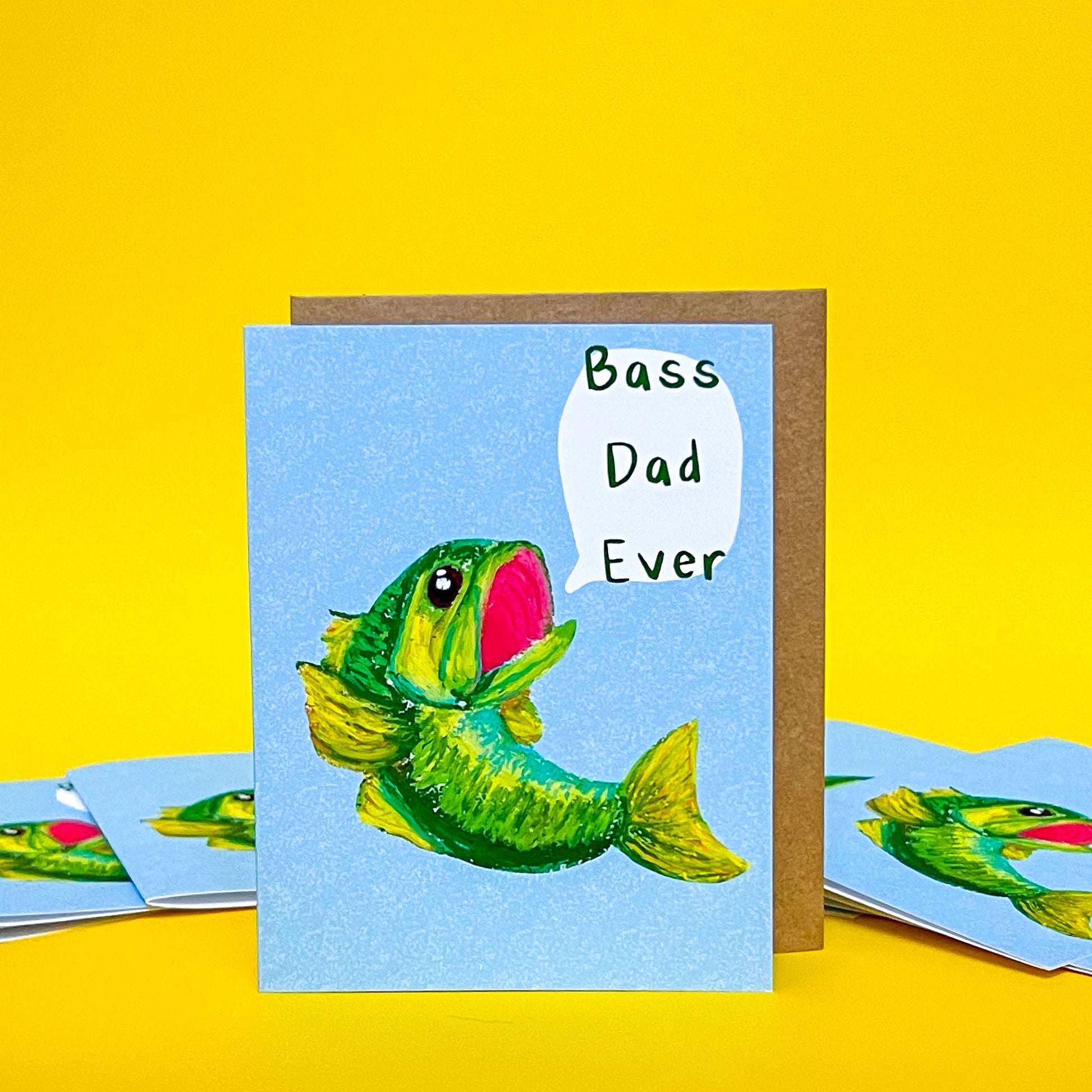 greeting card with green fish and text 'bass dad ever' against yellow background