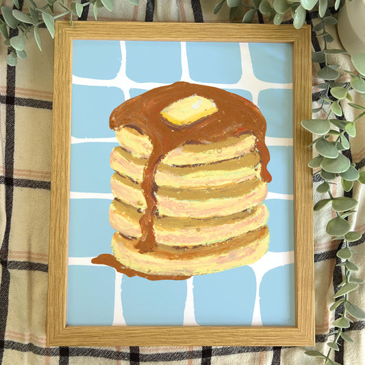Framed artwork of a stack of pancakes with syrup on a blue checkered background