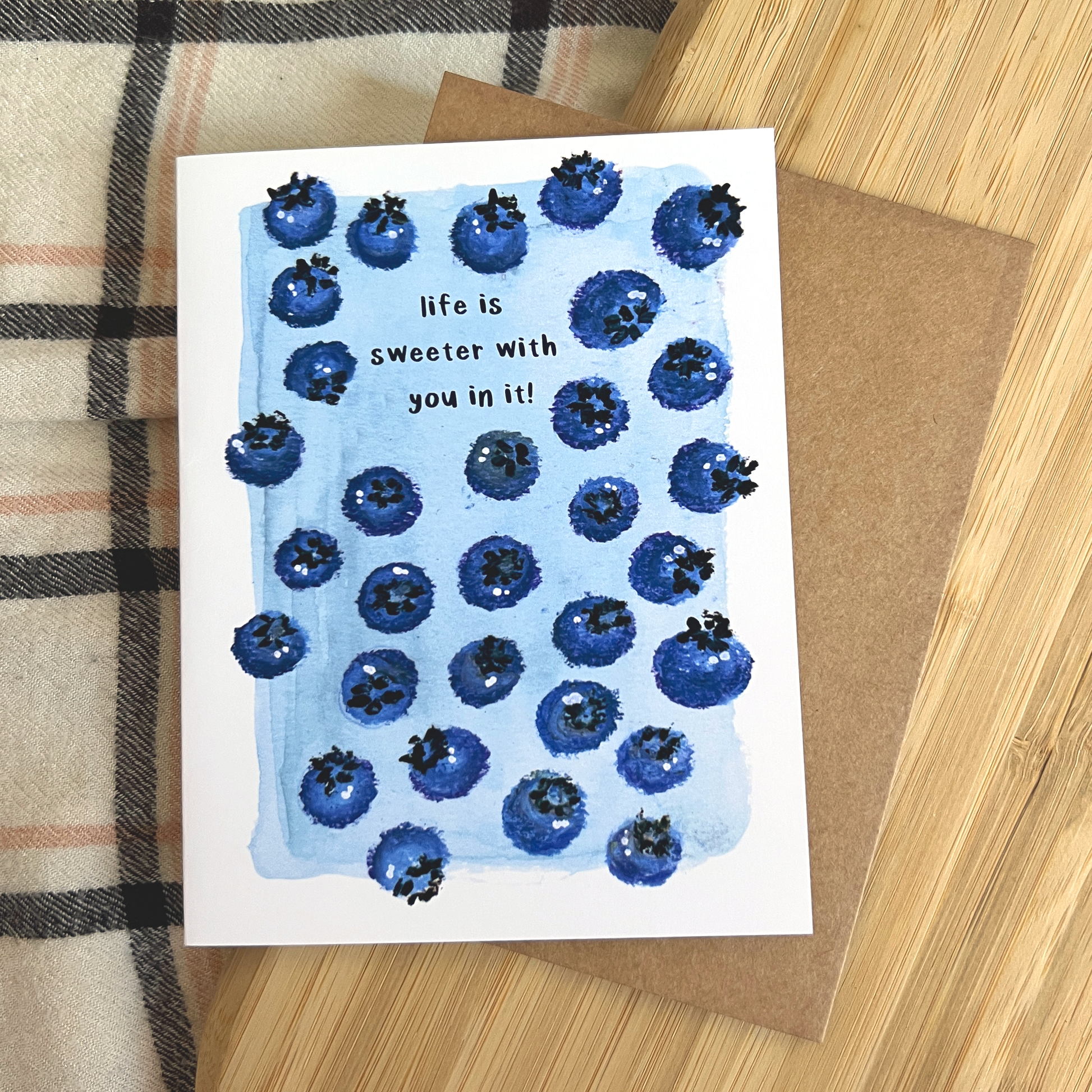Greeting card with blueberry design and text on a wooden surface
