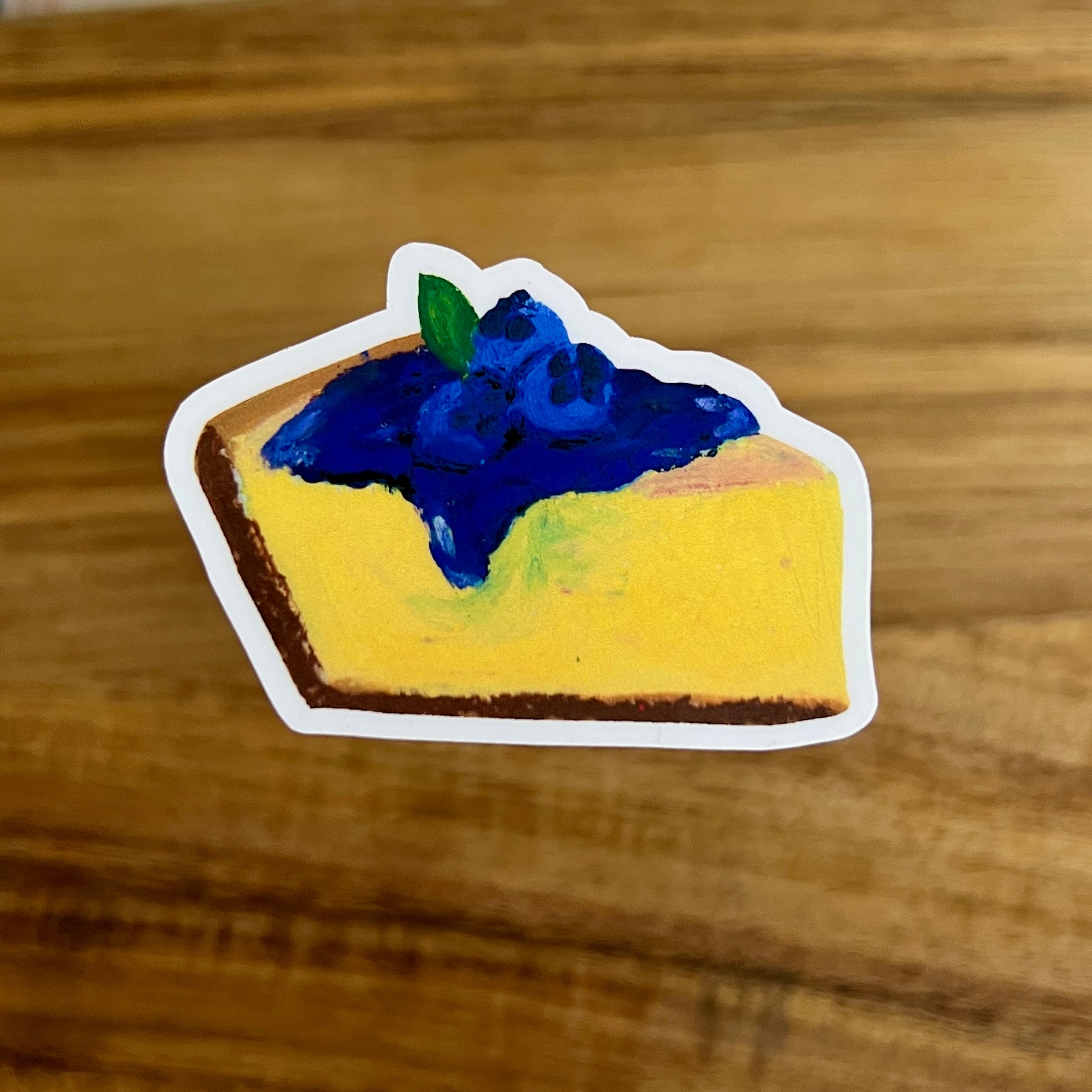 Sticker of a slice of pie with blueberry topping on a wooden surface