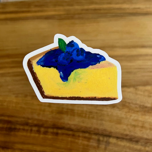 Sticker of a slice of pie with blueberry topping on a wooden surface