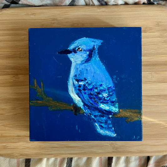 Painting of a blue bird on a blue background, placed on a wooden surface.