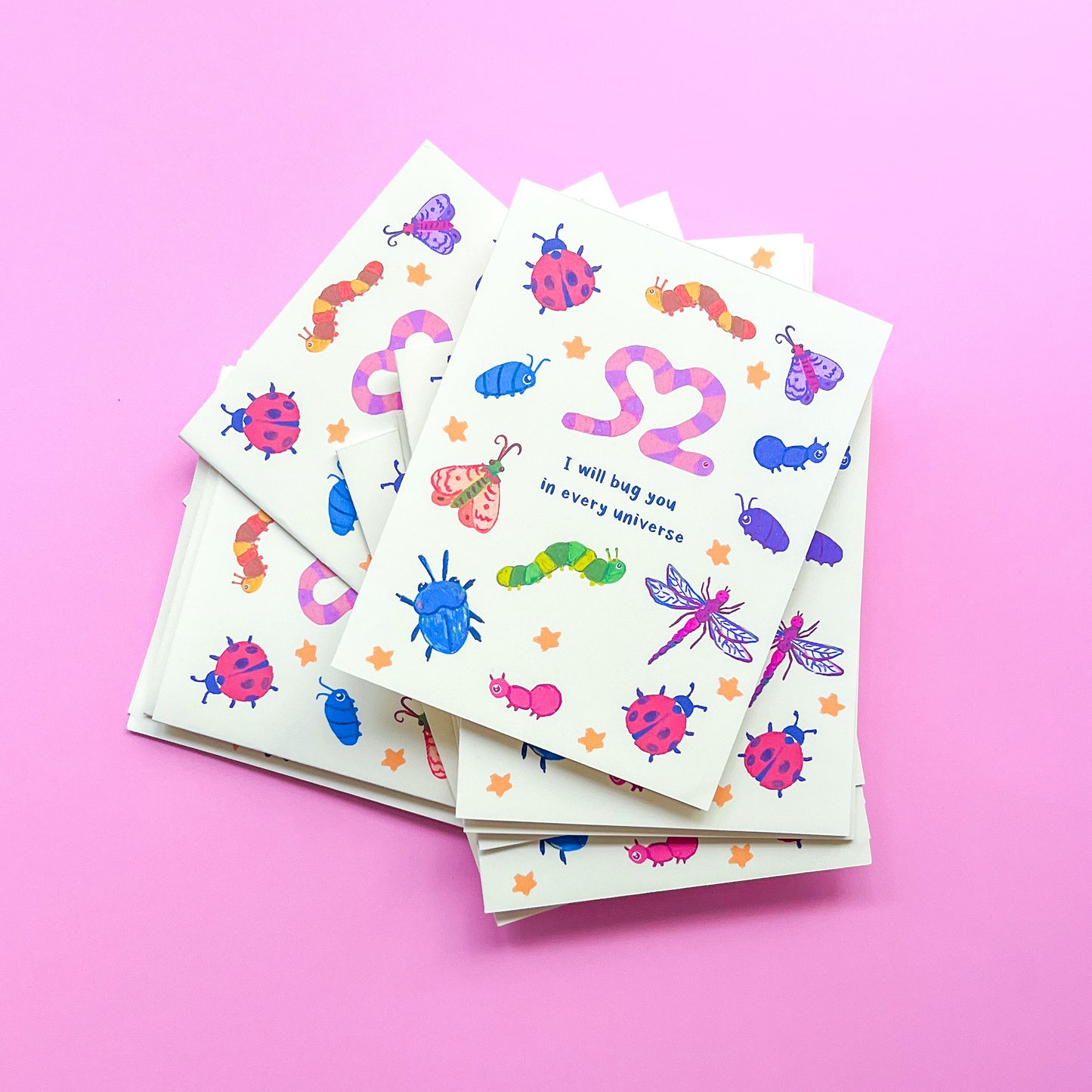 stack of greeting cards with an illustration of various bugs and text 'I will bug you in every universe' on pink background