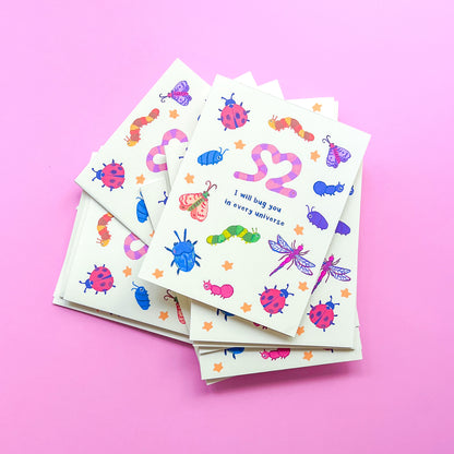 stack of greeting cards with an illustration of various bugs and text 'I will bug you in every universe' on pink background