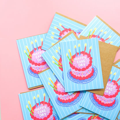 stack of birthday cards with cake illustration and text 'happy cake day' against a pink background