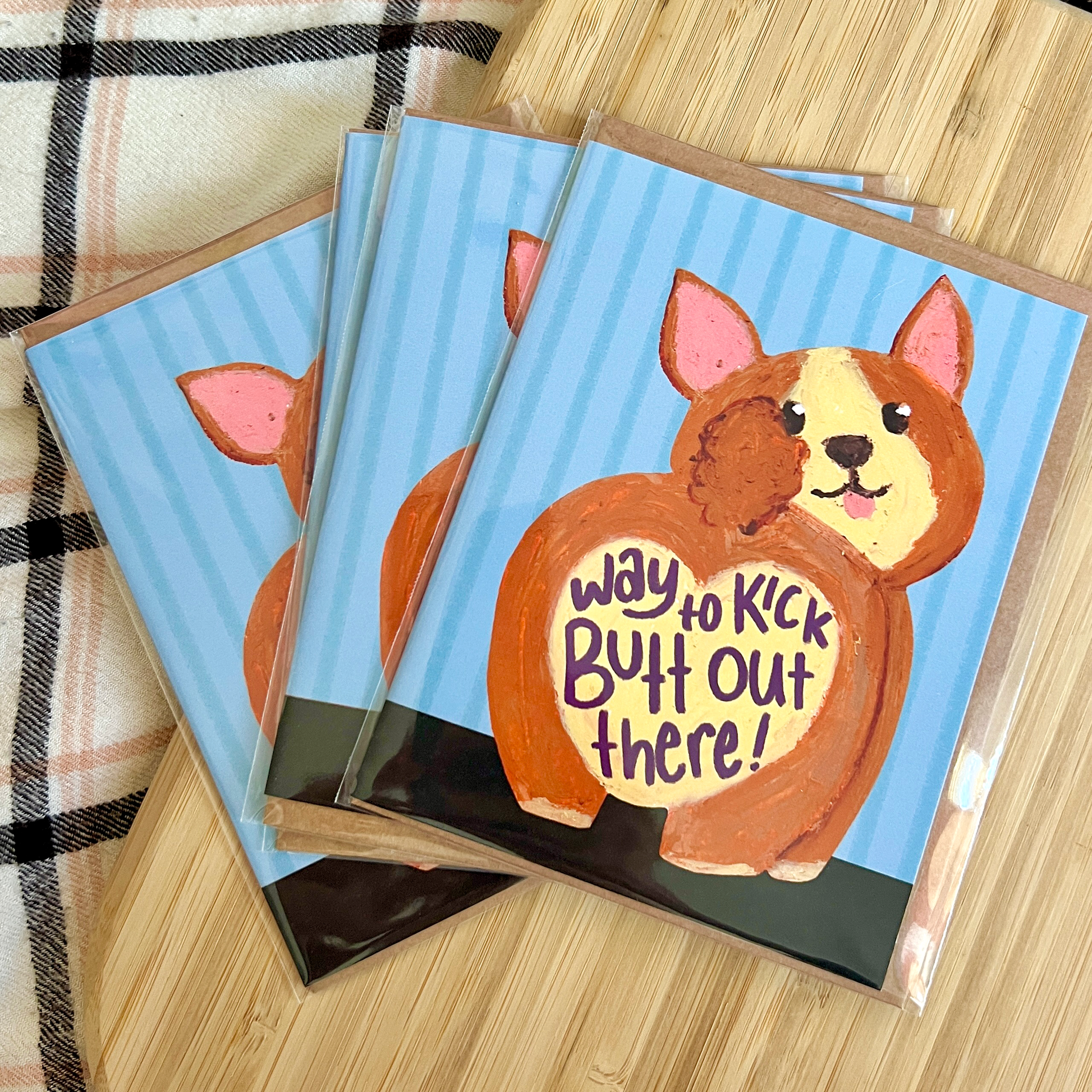 three carda with a drawn corgi with heart shaped butt on a blue striped background with text 'way to kick butt out there'