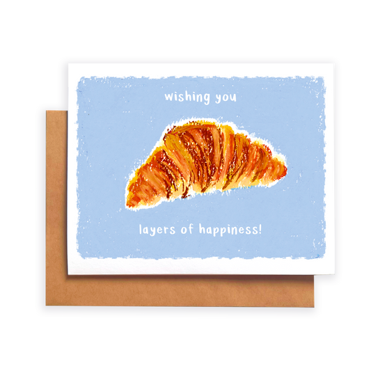 Greeting card with a croissant illustration and text 'wishing you layers of happiness' on a blue background
