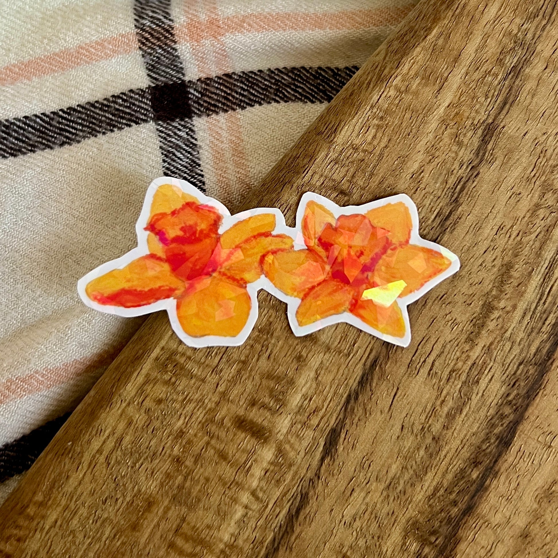 Two orange floral stickers on a wooden surface with a plaid fabric background