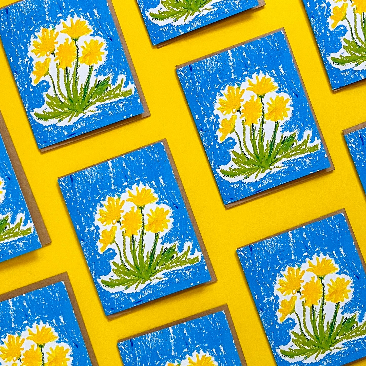 Pattern of greeting cards with yellow floral designs on a blue background, arranged on a yellow surface.