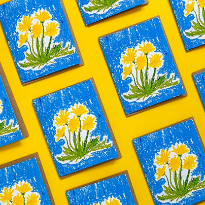 Pattern of greeting cards with yellow floral designs on a blue background, arranged on a yellow surface.