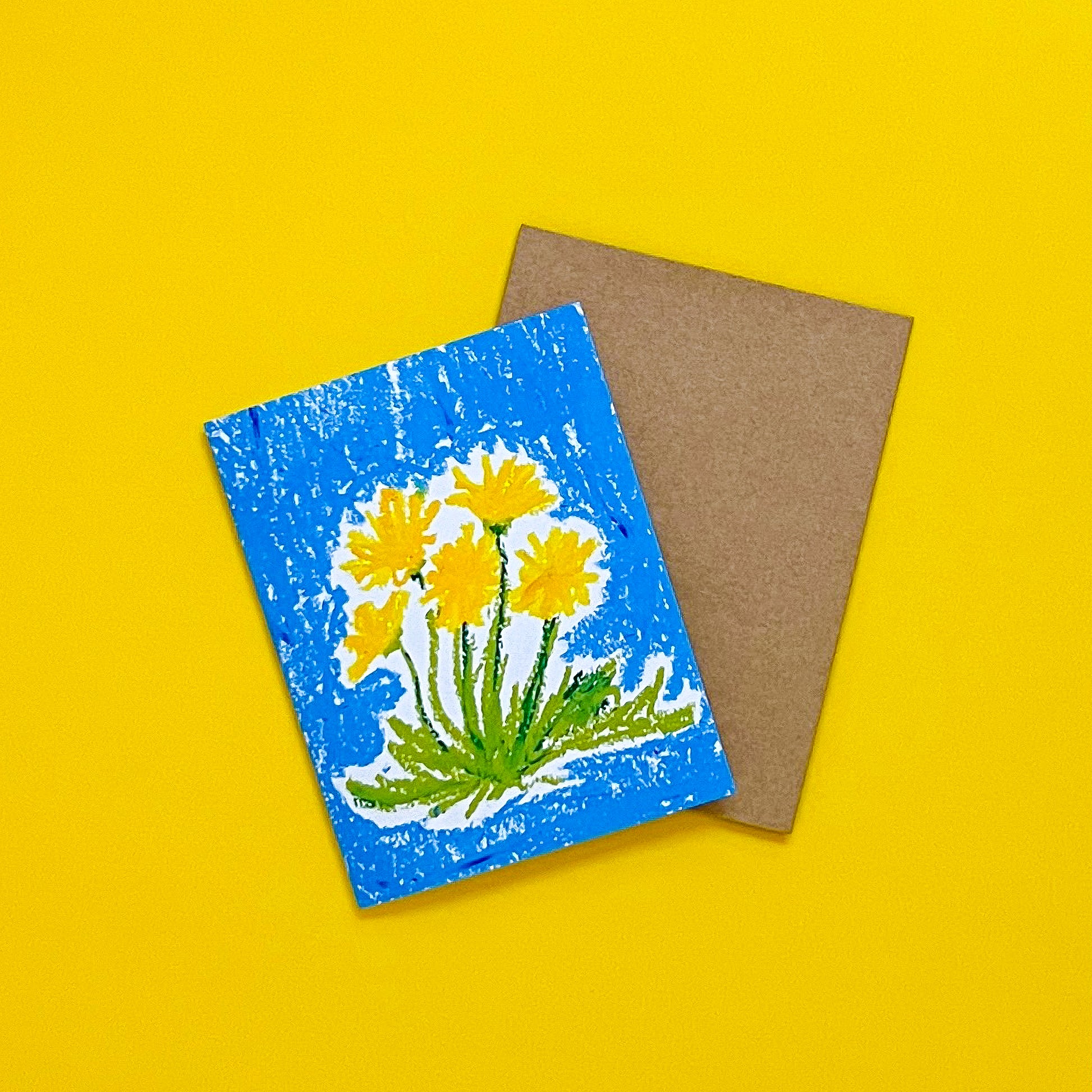 Card with yellow floral design on blue background and brown envelope on yellow background