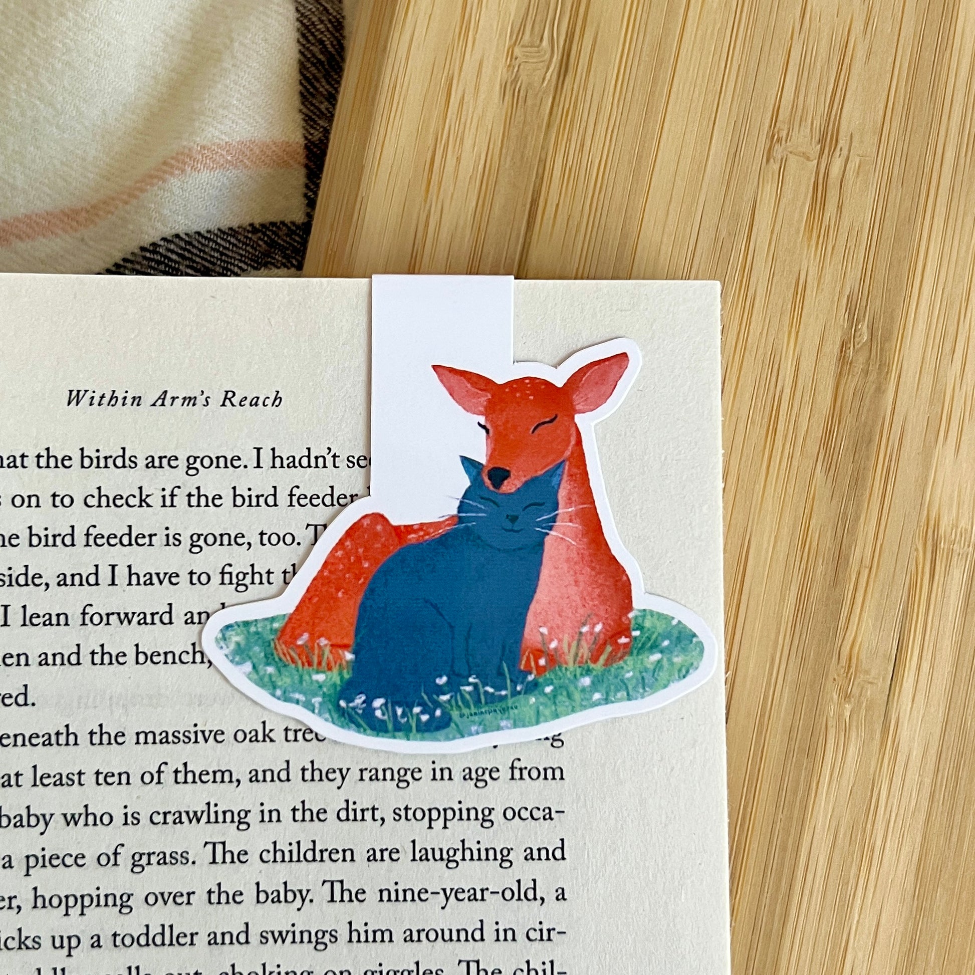 Sticker of a deer and a cat on a book page with a wooden surface in the background