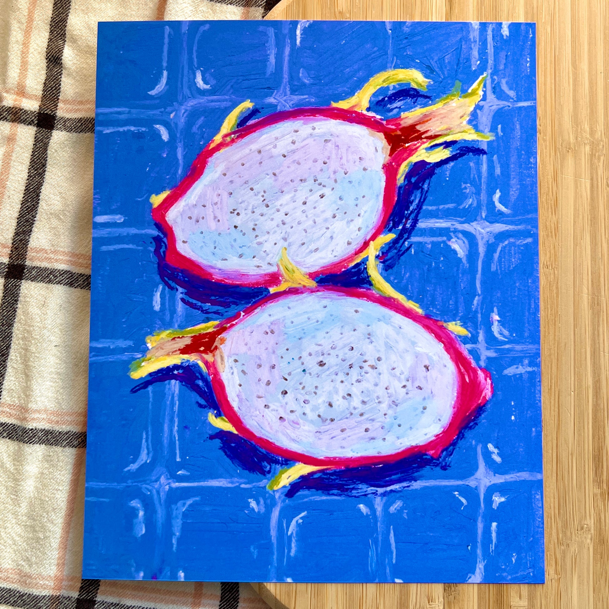 illustrated dragon fruit halved with blue tiled background on wooden and plaid surface