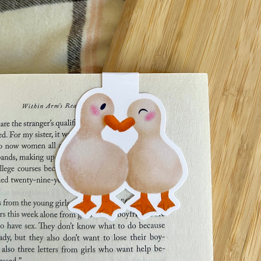 two illustrated ducks snuggling marking a book page on a wooden surface