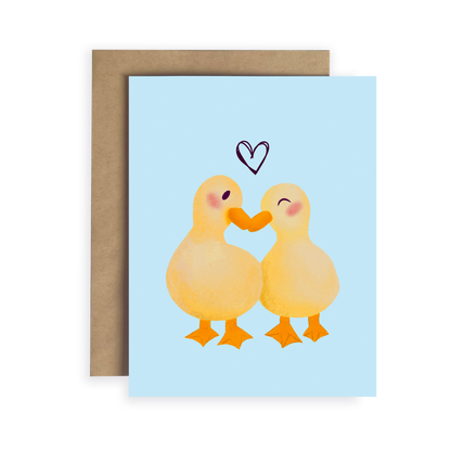 Greeting card with two ducks holding hands and a heart above them on a light blue background.