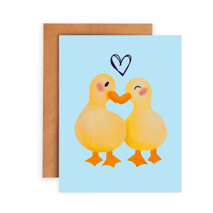 Greeting card with two ducks embracing and a heart above them on a light blue background.