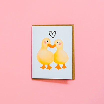 Card with two ducks hugging and a heart on a pink background