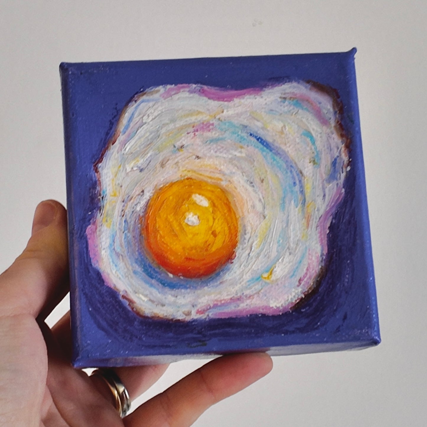 hand holding a fried egg painting on purple background