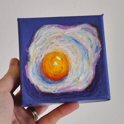 hand holding a fried egg painting on purple background