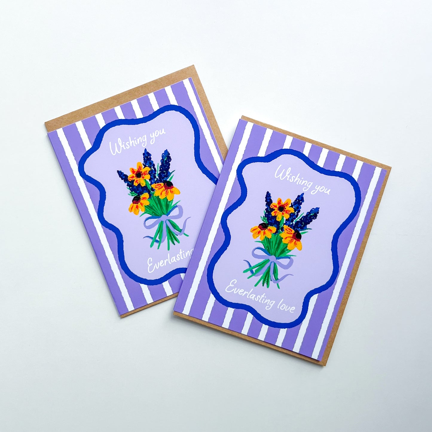 two wedding cards with hand drawn flowers and text 'wishing you everlasting love' on a purple striped background with Kraft envelope against white background