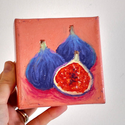 Small painting of blue and red figs held by a hand on a white background