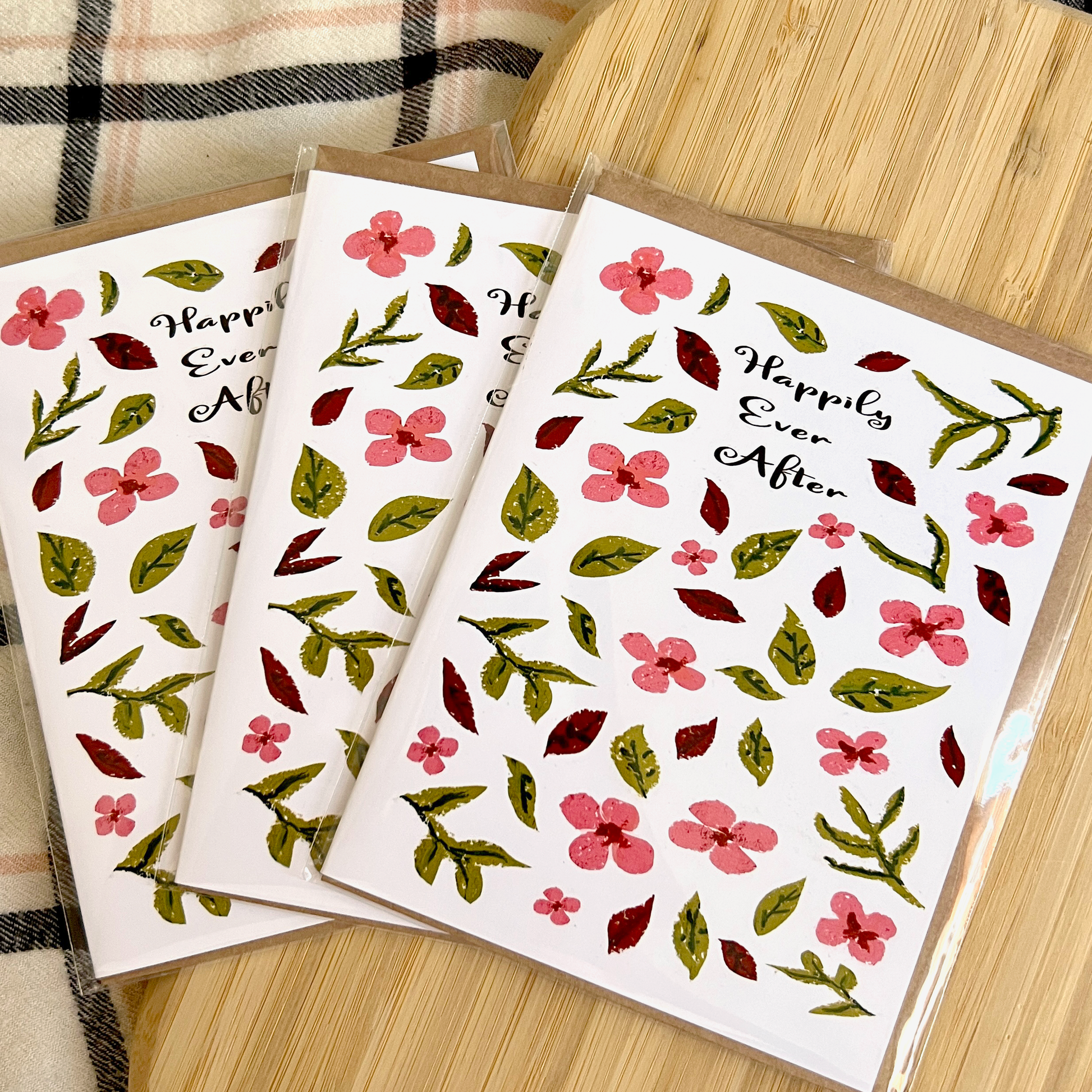 Three greeting cards with floral designs and 'Happily Ever After' text on a wooden surface.