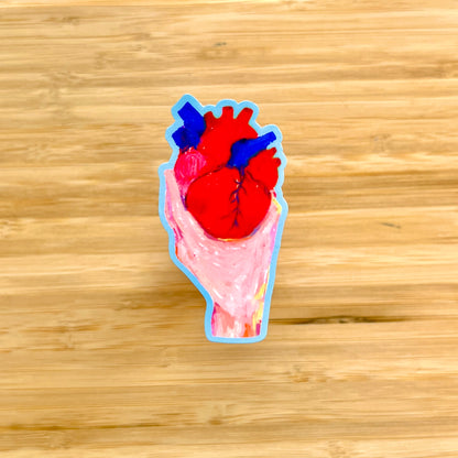 Sticker of a hand holding human heart on a wooden surface