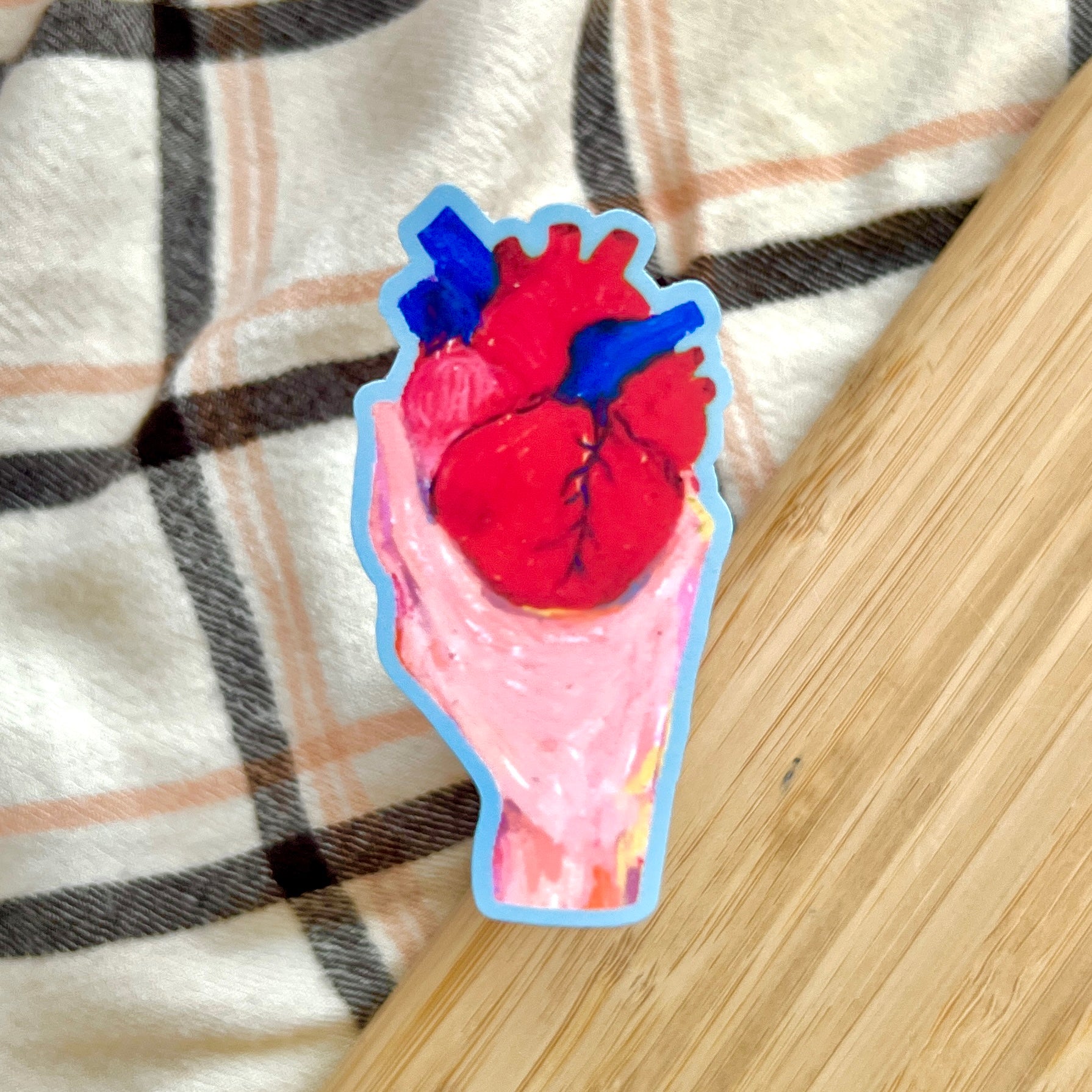 Sticker of a hand holding  human heart on a plaid fabric background