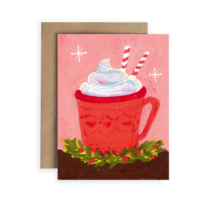 Greeting card with a red mug of hot chocolate, whipped cream, and candy canes on a pink background.