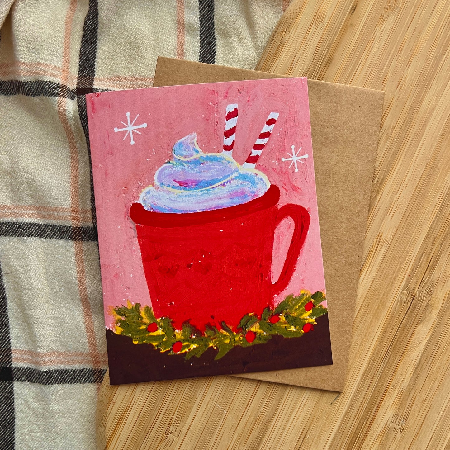 Card with a red mug of hot chocolate and whipped cream on a wooden surface.