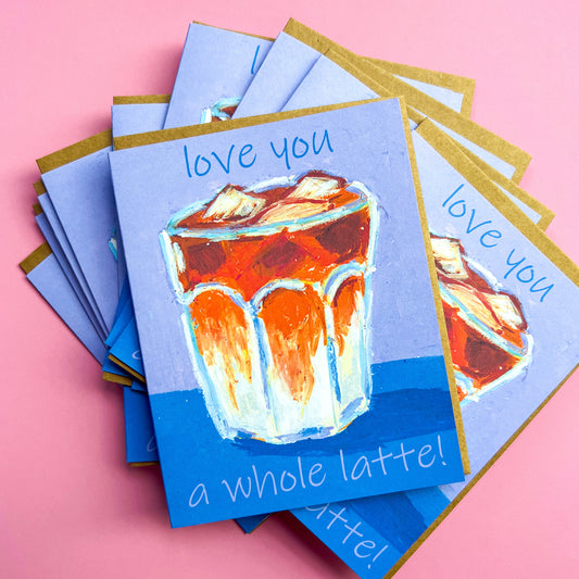 Stack of greeting cards with a drawing of an iced latte and text 'love you a whole latte!' on a pink background