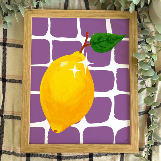 Framed artwork of a yellow lemon with green leaves on a purple and white patterned background.