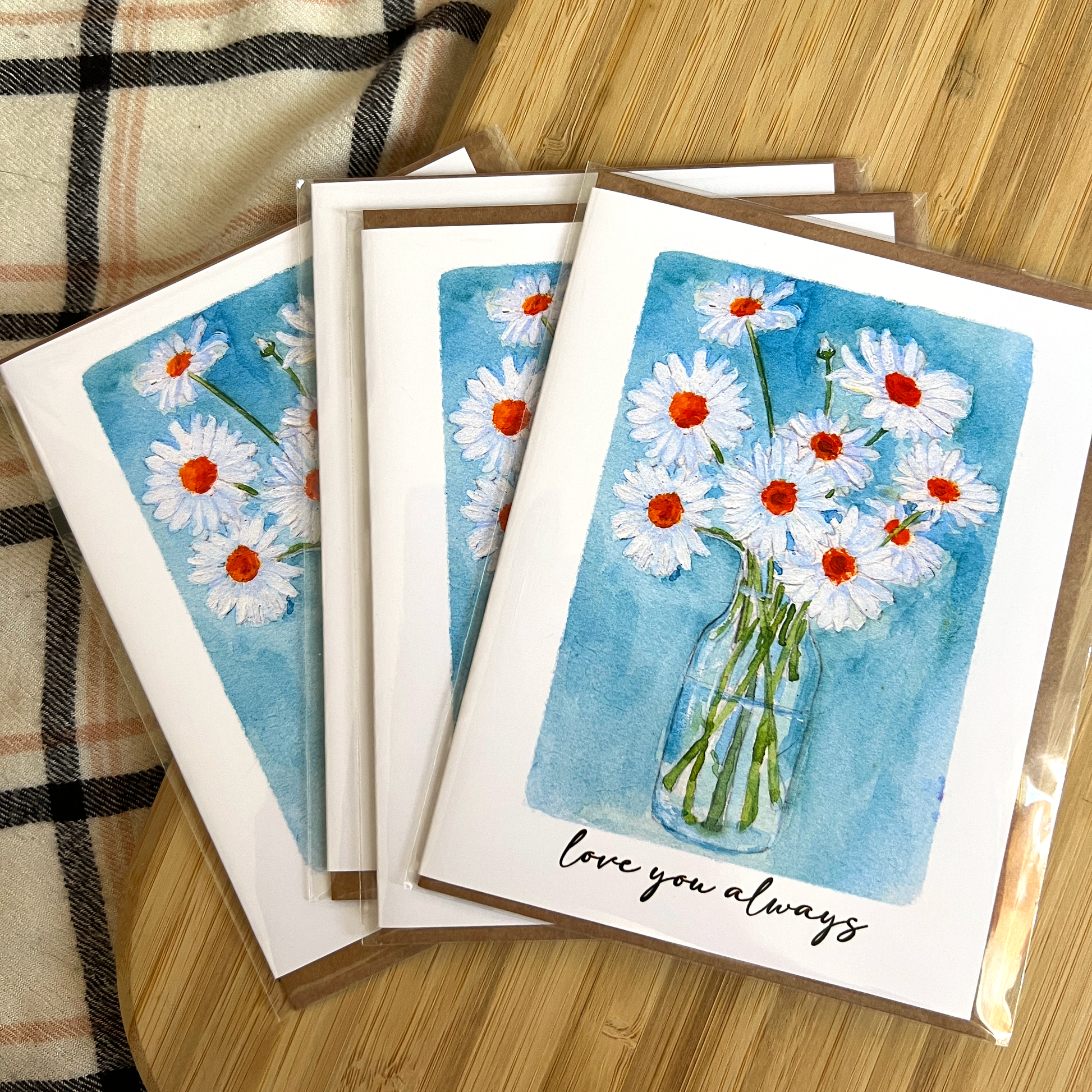 Set of greeting cards with floral design and 'love you always' text on a wooden surface.