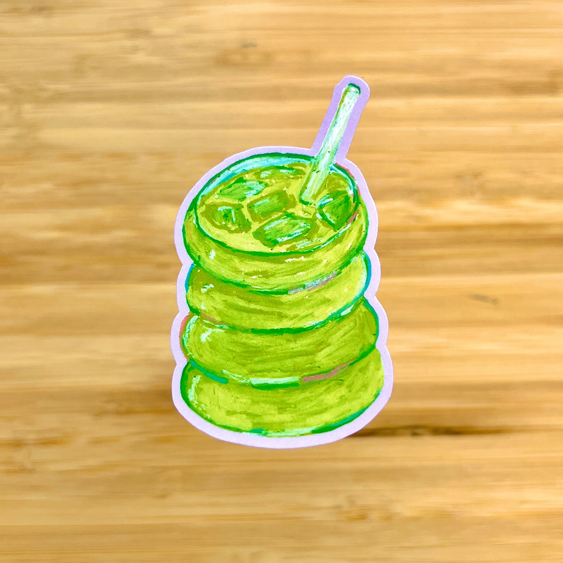 Sticker of a green matcha with a straw on a wooden background