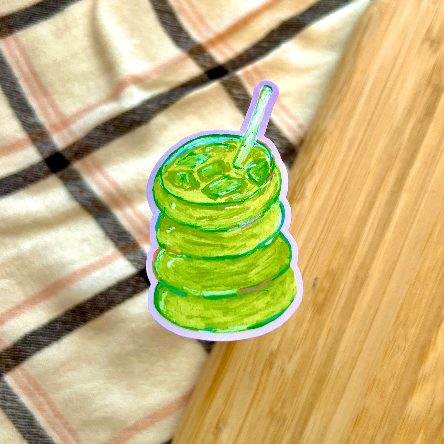 Illustration of a green matcha with a straw on a plaid fabric background