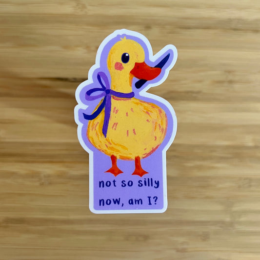 Sticker of a yellow duck with a purple bow and text on a wooden surface