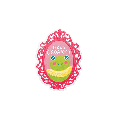 Sticker with a cartoon frog in a decorative frame with text 'okey croaky' on a white background