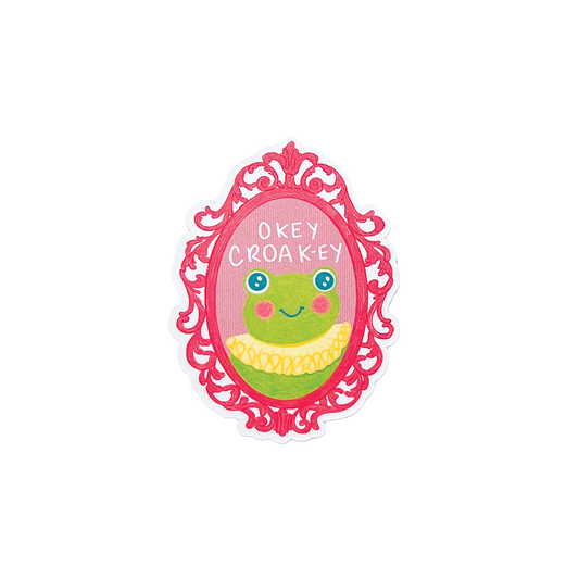 Sticker with a cartoon frog in a decorative frame with text 'okey croaky' on a white background