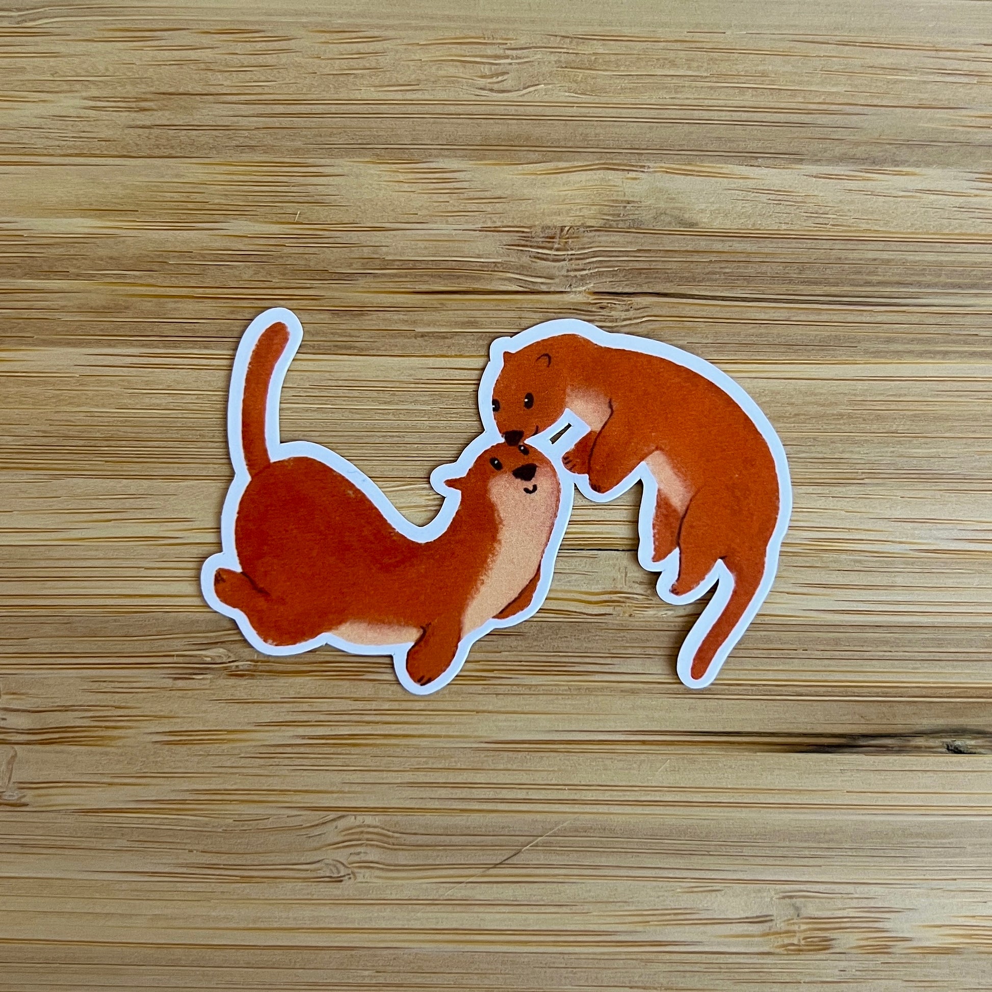 Two otter stickers on a wooden surface