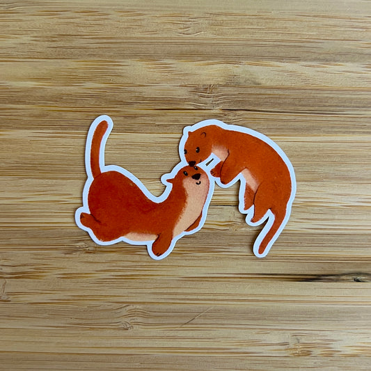 Two otter stickers on a wooden surface