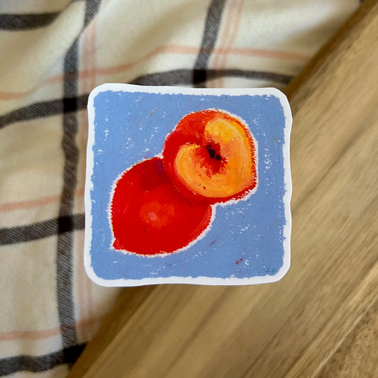 Small painting of two peaches on a blue background, placed on a checkered fabric surface.