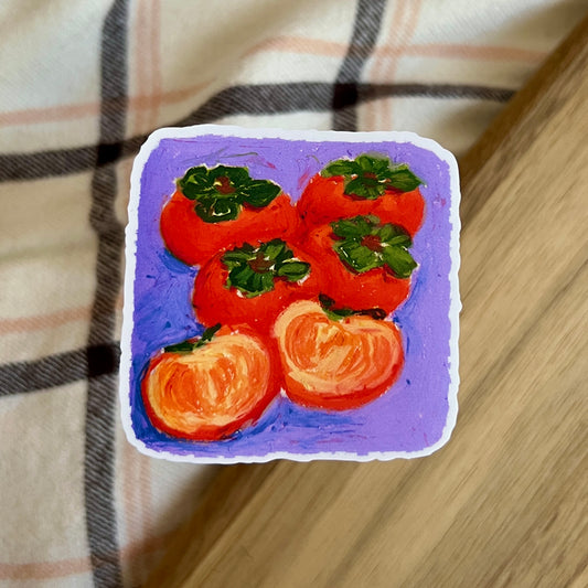 Sticker with a drawing of persimmons on a purple background, placed on a checkered fabric surface.