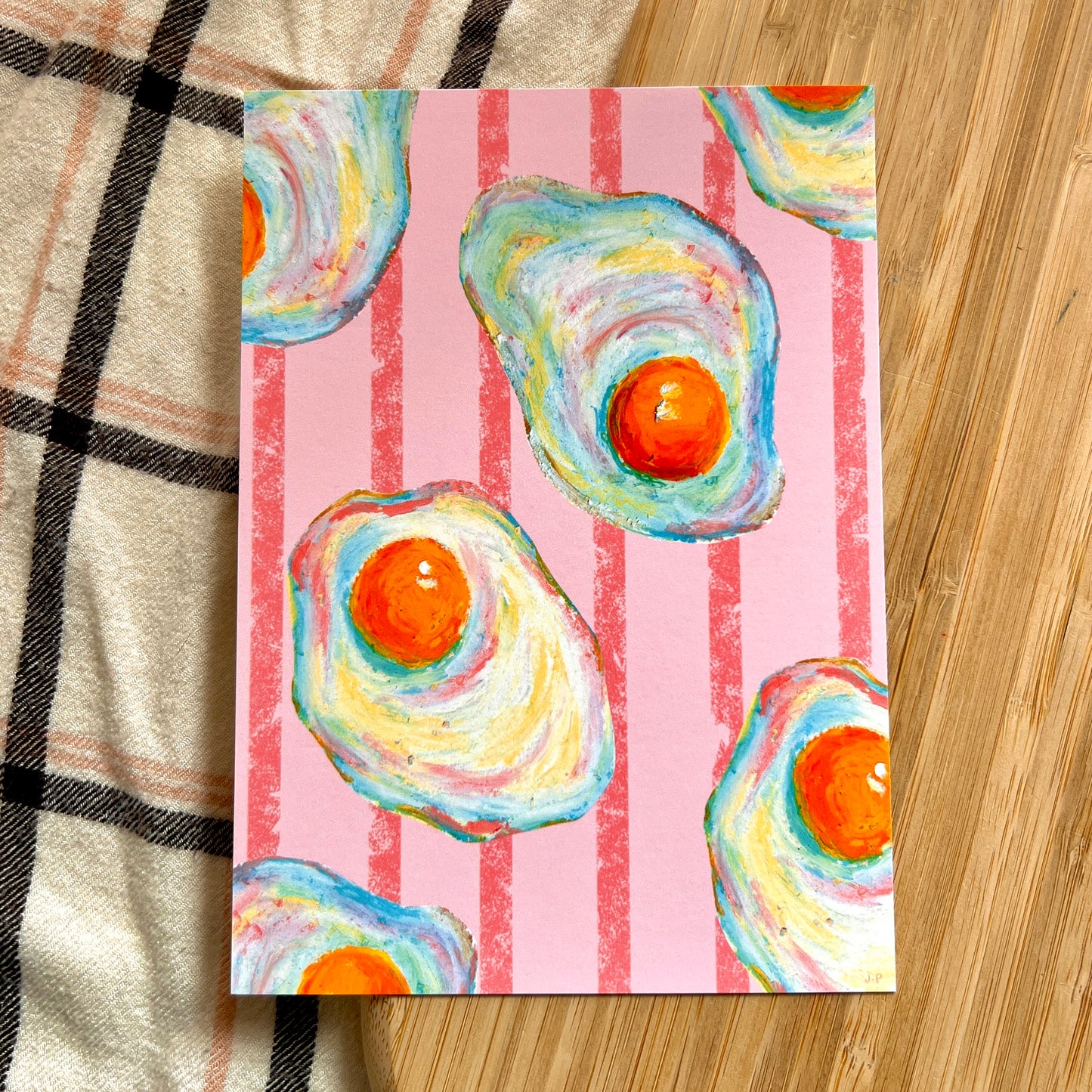 illustrated fried eggs with pink striped background on wooden and plaid surface