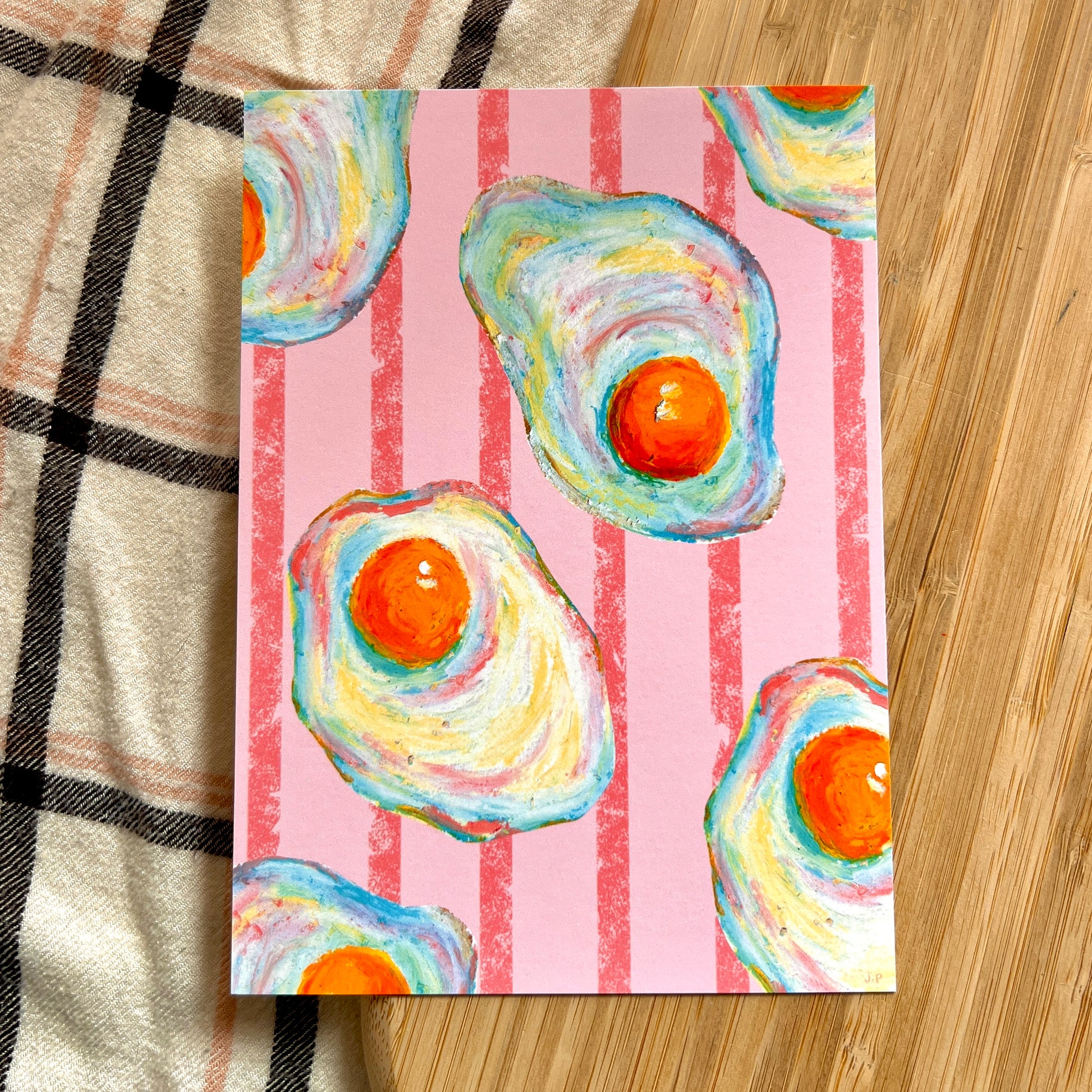 illustrated fried eggs with pink striped background on wooden and plaid surface