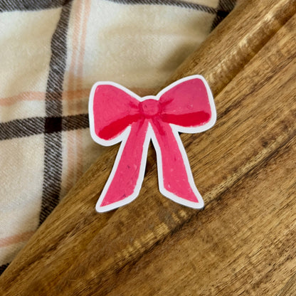 Pink bow sticker on a wooden surface with plaid fabric in the background