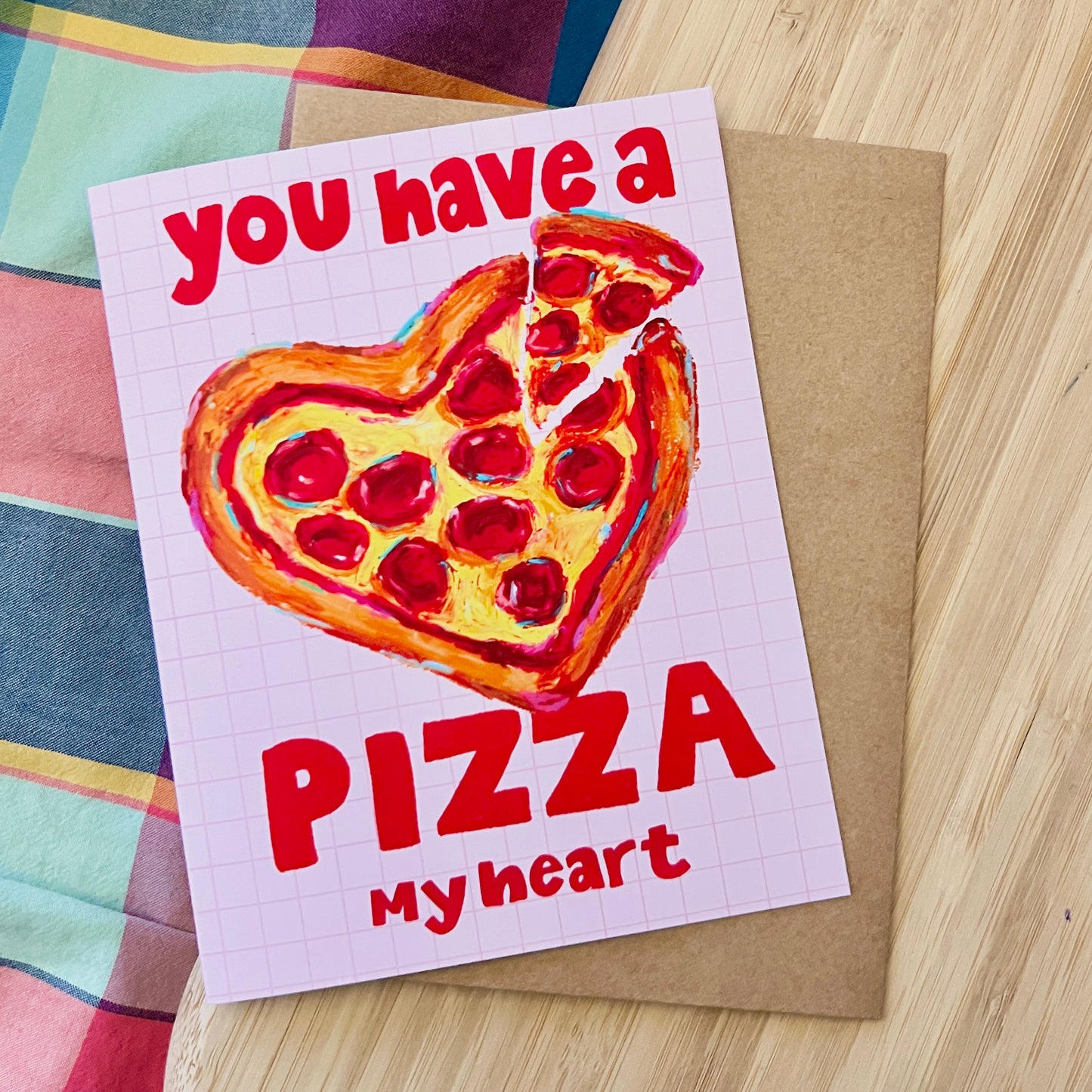 Card with a heart-shaped pizza illustration and text 'you have a pizza my heart' on a wooden surface.