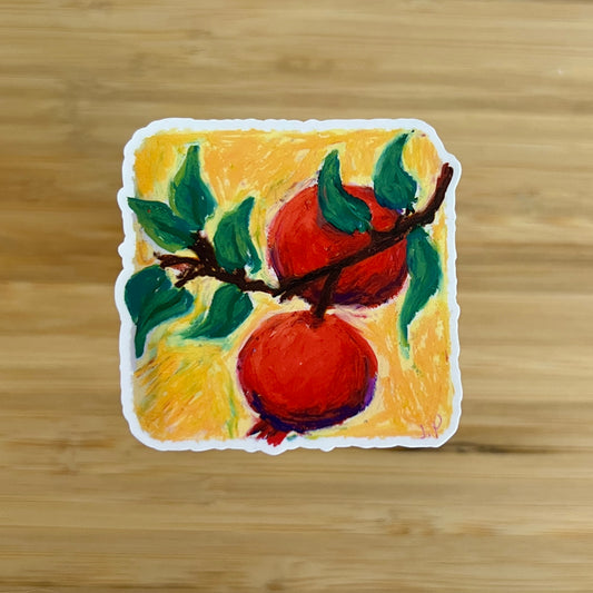 Painting of two red pomegranates on a branch with green leaves on a yellow background, placed on a wooden surface.