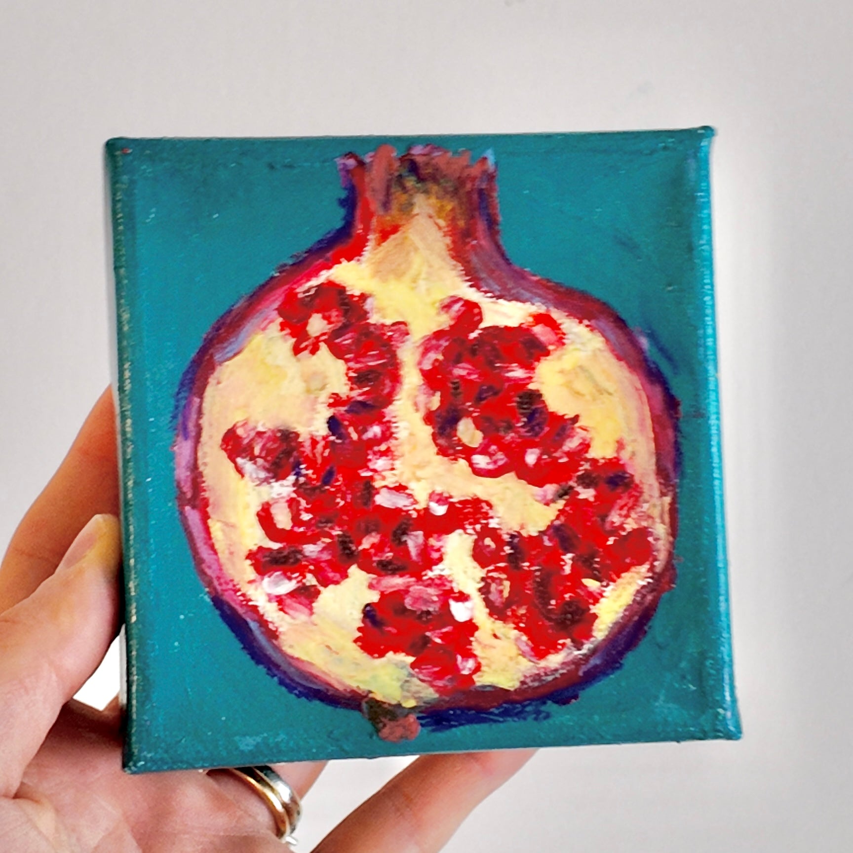 Small painting of a pomegranate held by a hand against a light background