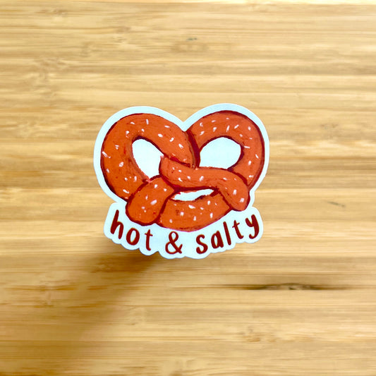 Sticker of a pretzel with 'hot & salty' text on a wooden surface